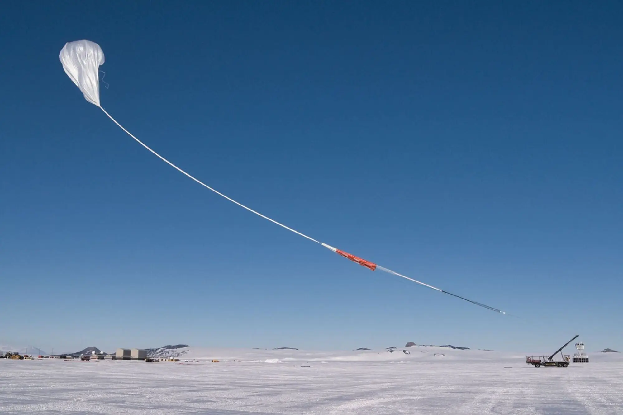 A white balloon with a long tether hovering above the icy ground