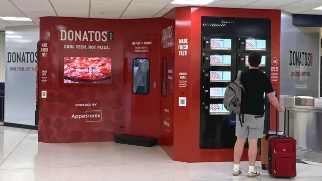 Koyu kırmızı renkli Donatos taze pizza otomatı, bir minibüs büyüklüğünde. Bir müşteri ekranına bakıyor.