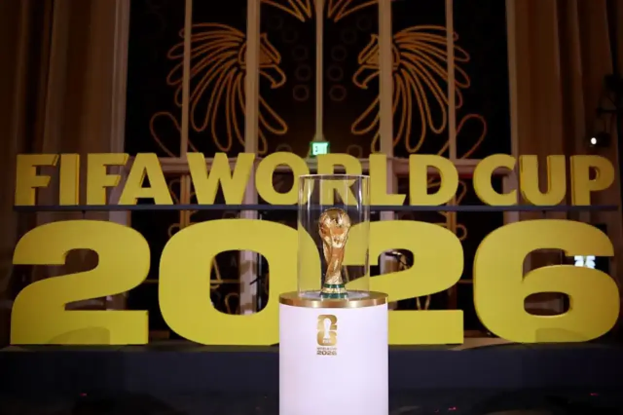 Arka planda FIFA Dünya Kupası 2026 logosunun yer aldığı bir fotoğrafta kupa bir camekanın içinde duruyor.